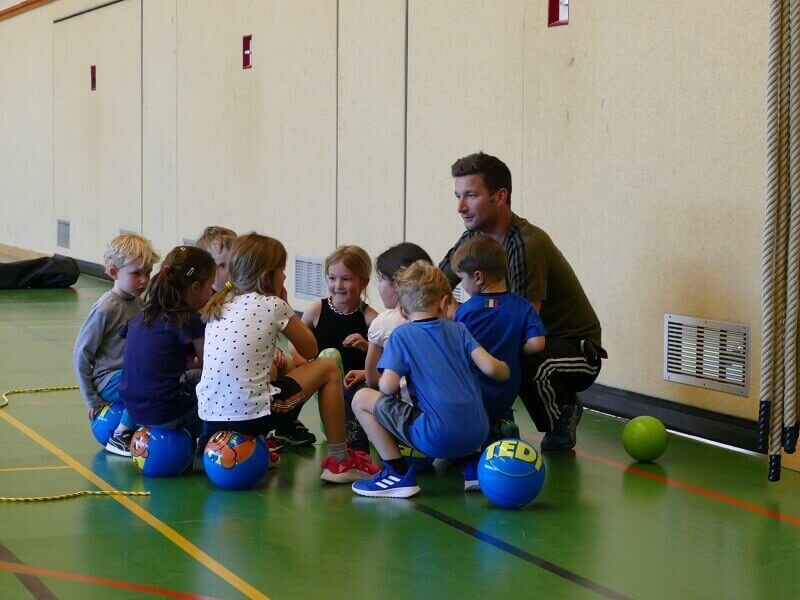 Kinder sitzen mit ihrem Übungsleiter auf Bällen in einer gemeinsamen Runde der Ballschule des TuS Mosella Schweich