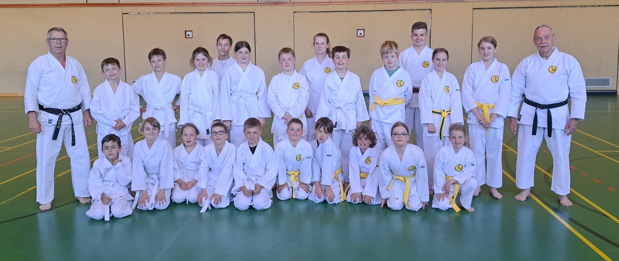 Kinder und Erwachsene in weißen Karateanzügen beim Gruppenfoto in der Sporthalle Kinder und Erwachsene in weißen Karateanzügen beim Gruppenfoto in der Sporthalle